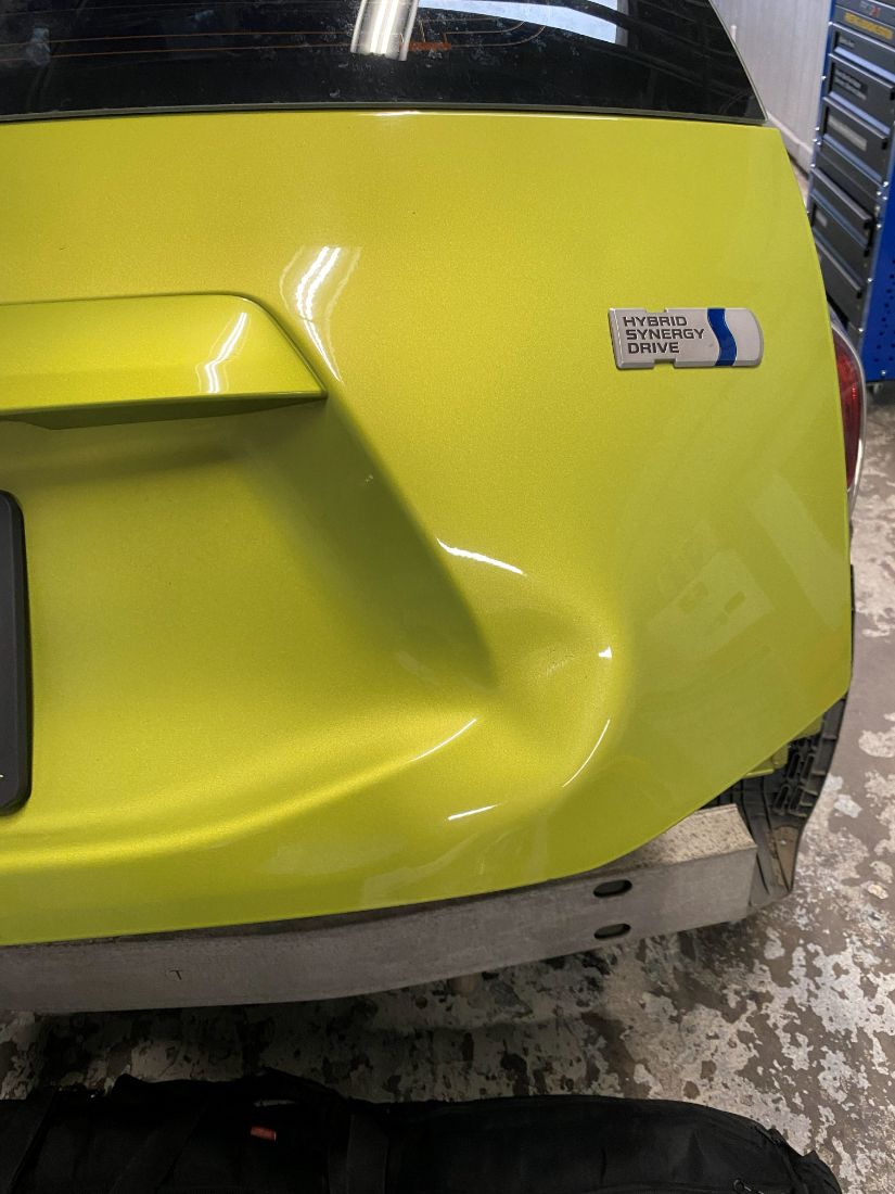 Dent on a yellow tailgate before repair