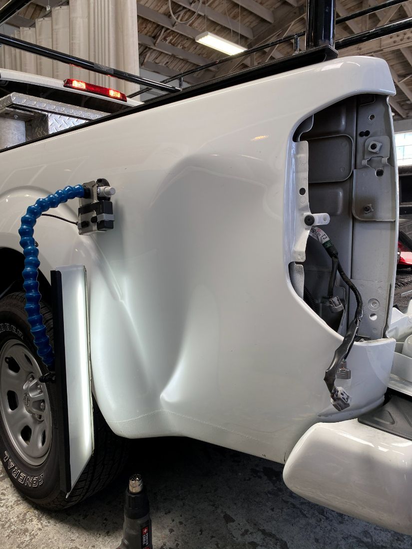 Large dent on a white truck bed before repair