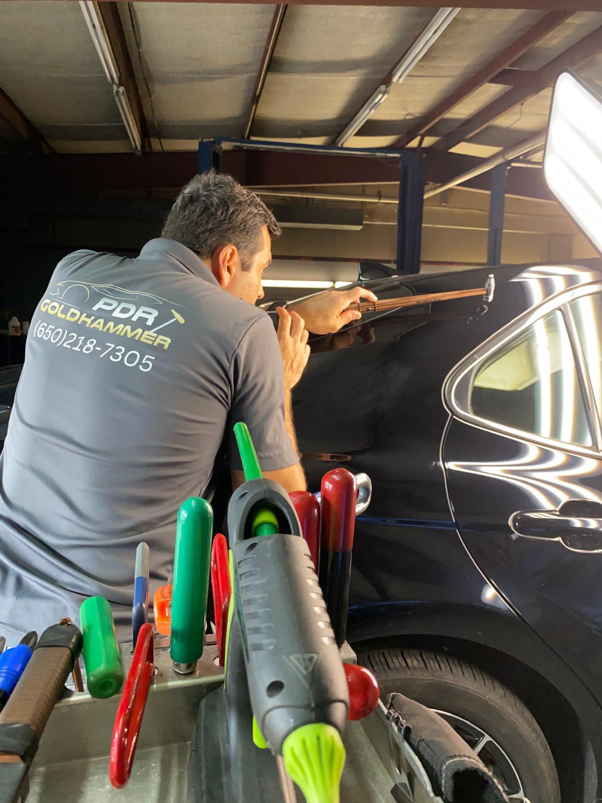 Marcus Gomes working a dent on a dark sedan with PDR rods