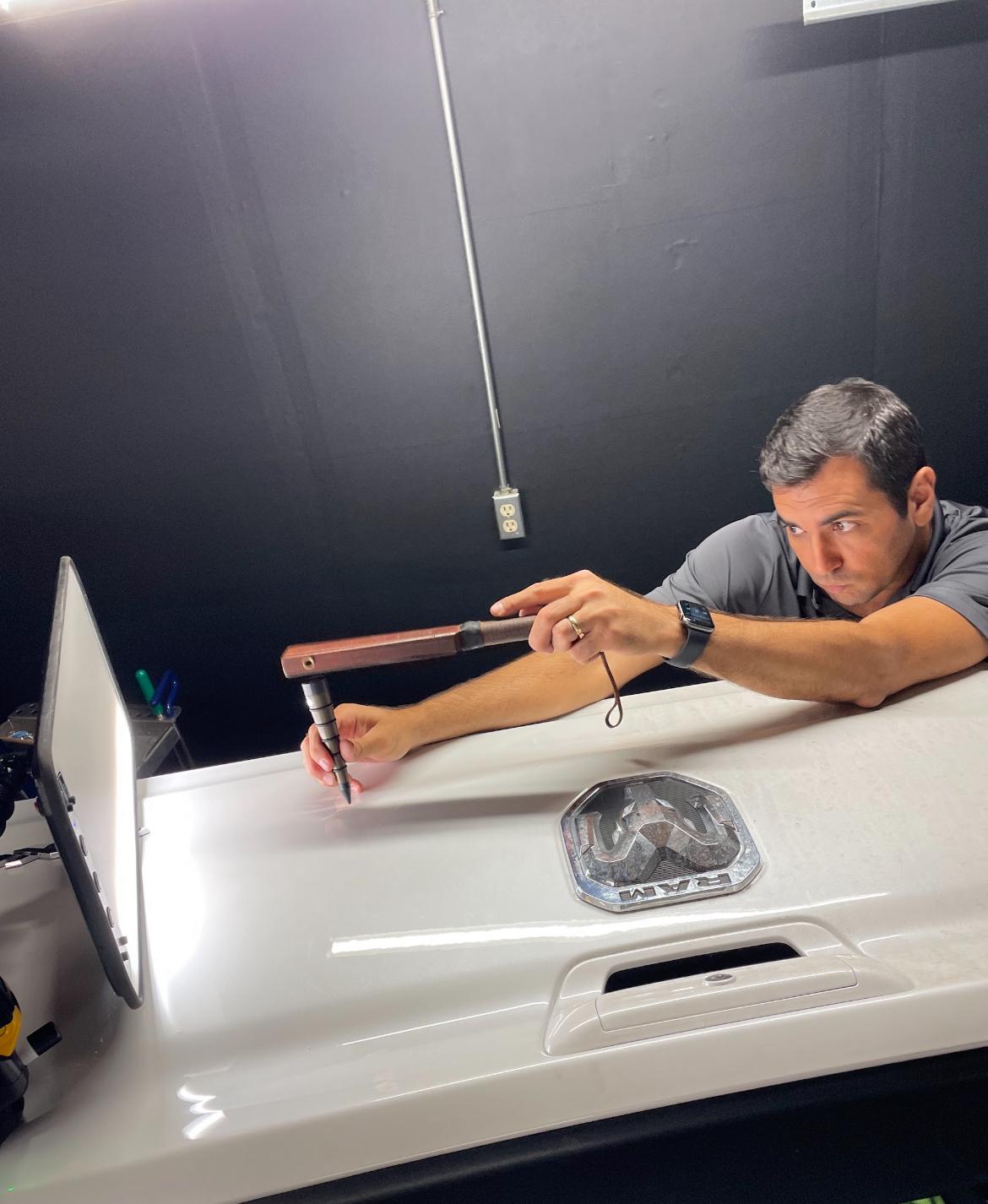 Marcus Gomes removing a dent from a truck tailgate under a reflection light board